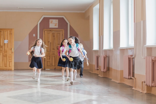 Young schoolchildren in uniforms running happily down a school hallway with backpacks.