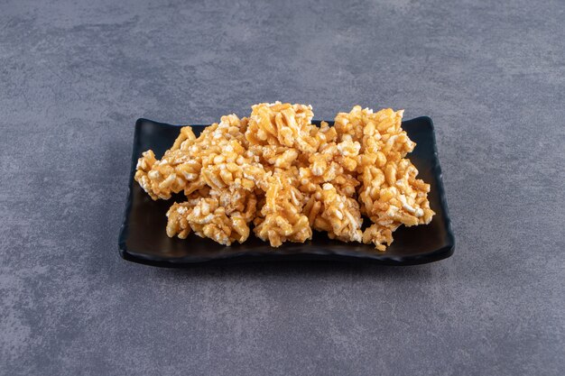 Clusters of puffed rice cereal coated in caramel sauce served on a black rectangular plate.